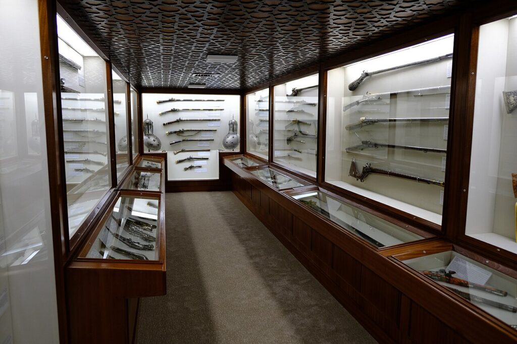 A long museum hallway lined with glass display cases containing numerous antique firearms and historical artifacts.