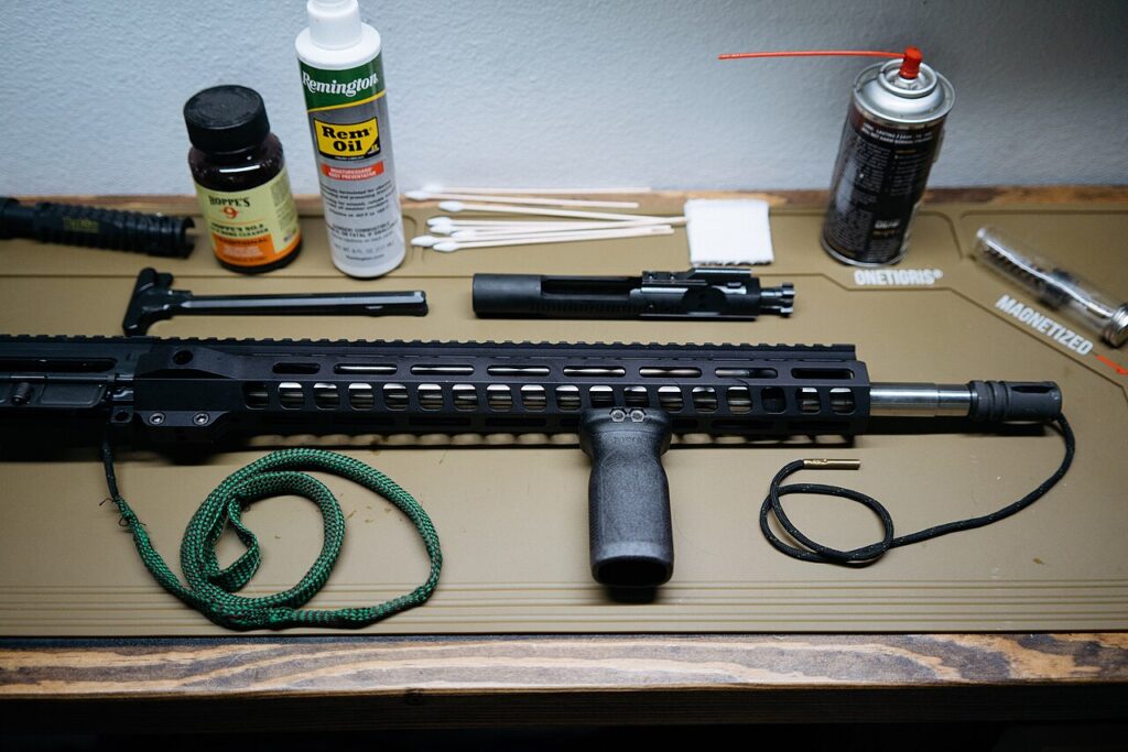 A rifle disassembled on a cleaning mat with bottles of gun oil, cleaning solvents, and a bore snake.