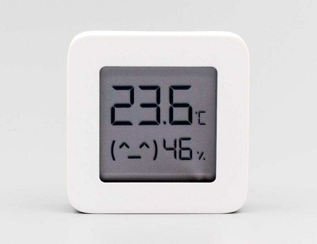A white digital temperature and humidity sensor displaying numerical readings on a clear screen.