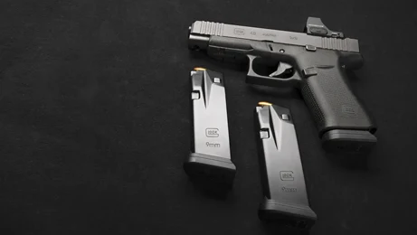 GLOCK press photograph of a pistol and two magazines displayed on a dark background.