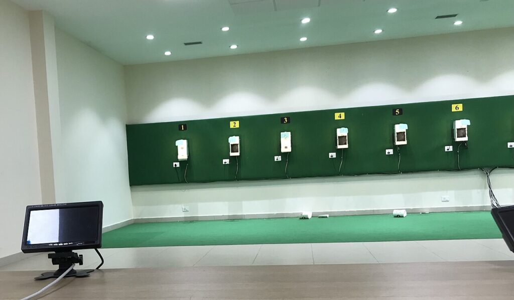 A modern indoor shooting range with green wall panels and digital target monitors for athletes.