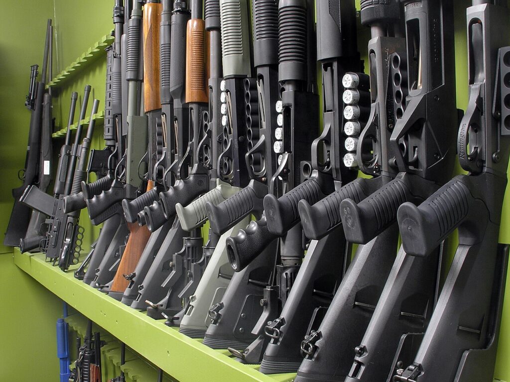 A row of various shotguns displayed on a rack, showcasing different barrel lengths and stock configurations.