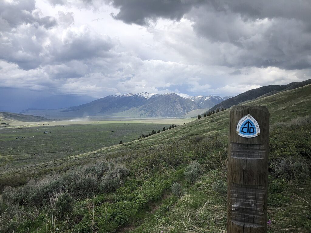 A sign for the Continental Divide Trail stands in a vast, open landscape with mountains in the distance.
