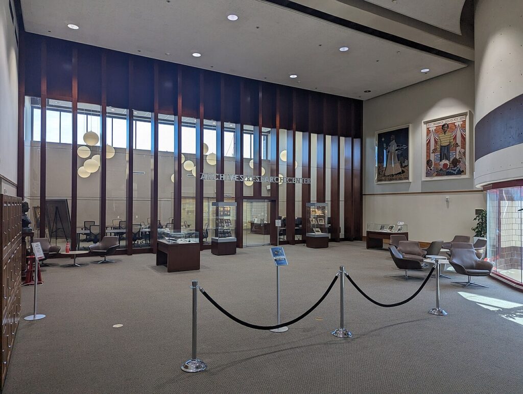 A spacious, modern research archive room with seating areas and glass display cases in a library.