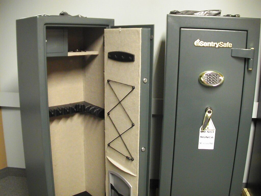 Two grey metal gun safes standing in a room, one open and one closed.