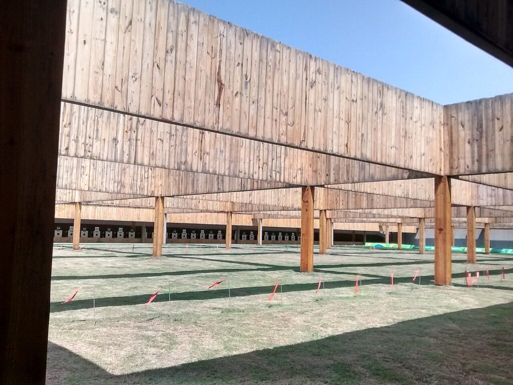 A wide, outdoor shooting range featuring wooden support beams and multiple target stations under a clear sky.
