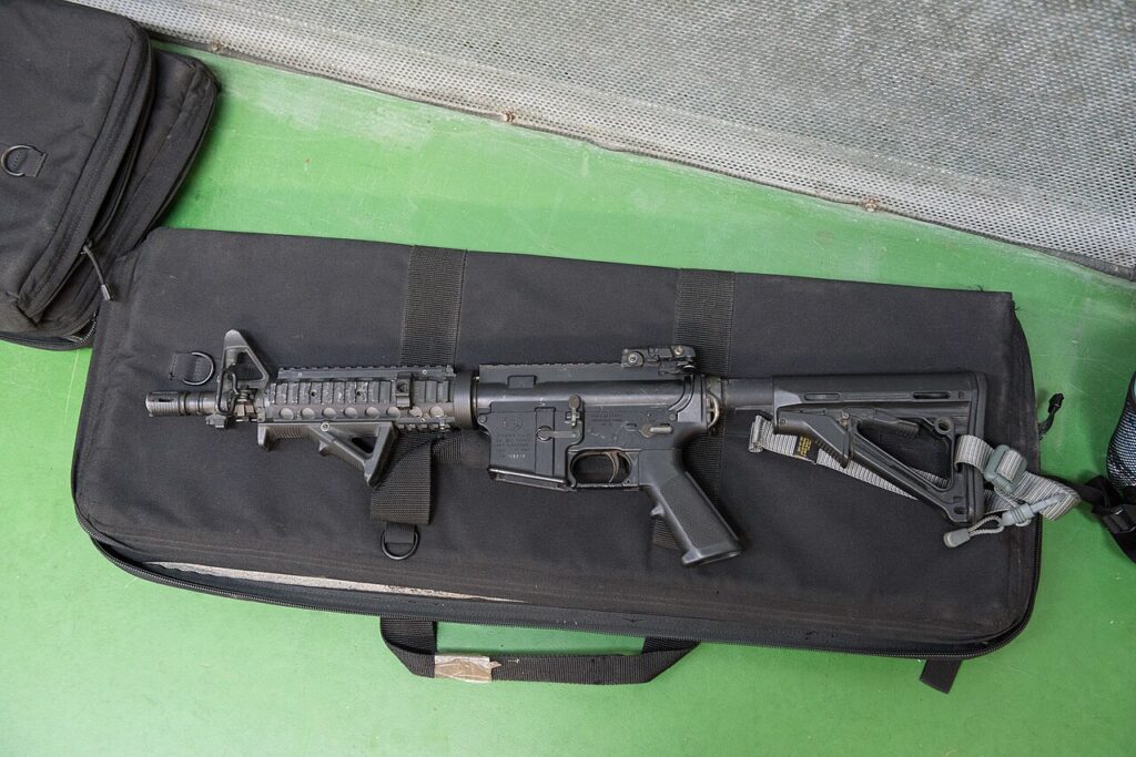 A black rifle resting on a black equipment bag at a shooting range.