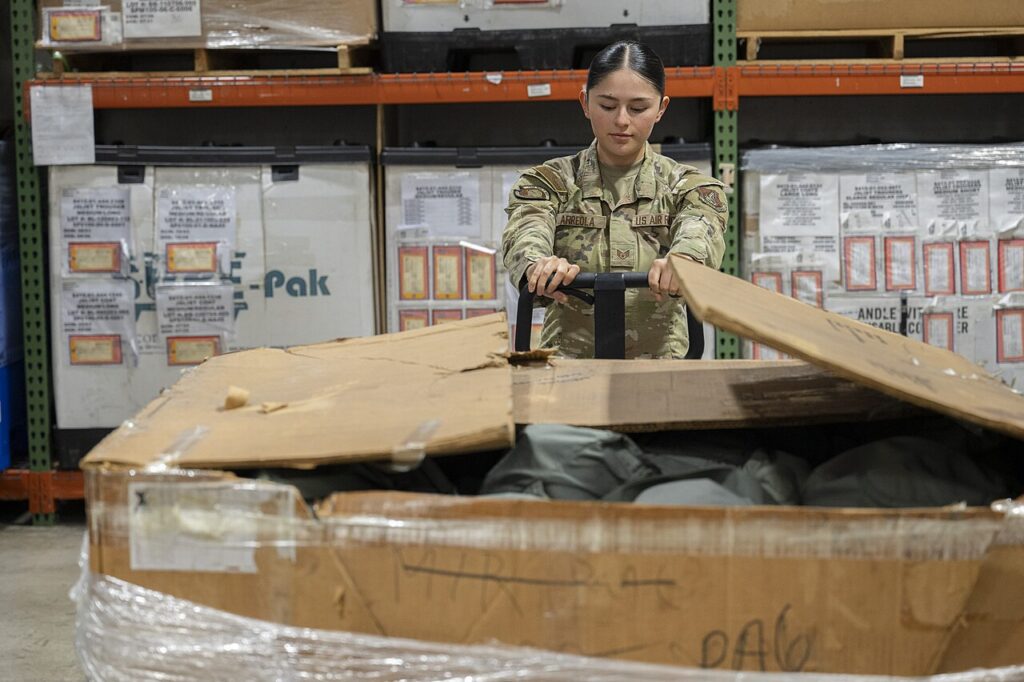 A U.S. Air Force logistics professional organizing and storing large supply crates in a warehouse setting.