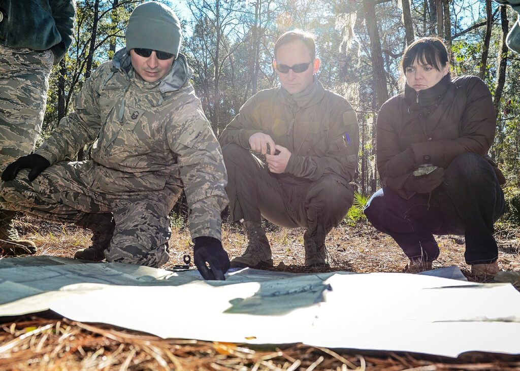 Three individuals outdoors in a wooded area examining a paper map together for navigation planning.