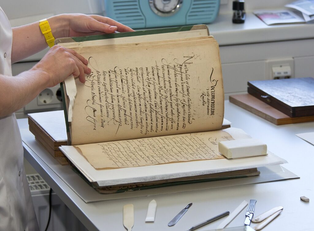 Hands carefully inspecting and organizing an old historical document on a clean desk with archival tools.