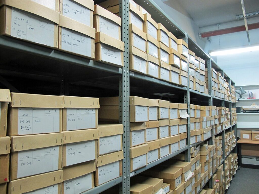 Rows of cardboard archival boxes stacked on metal shelving units inside a climate-controlled storage facility.