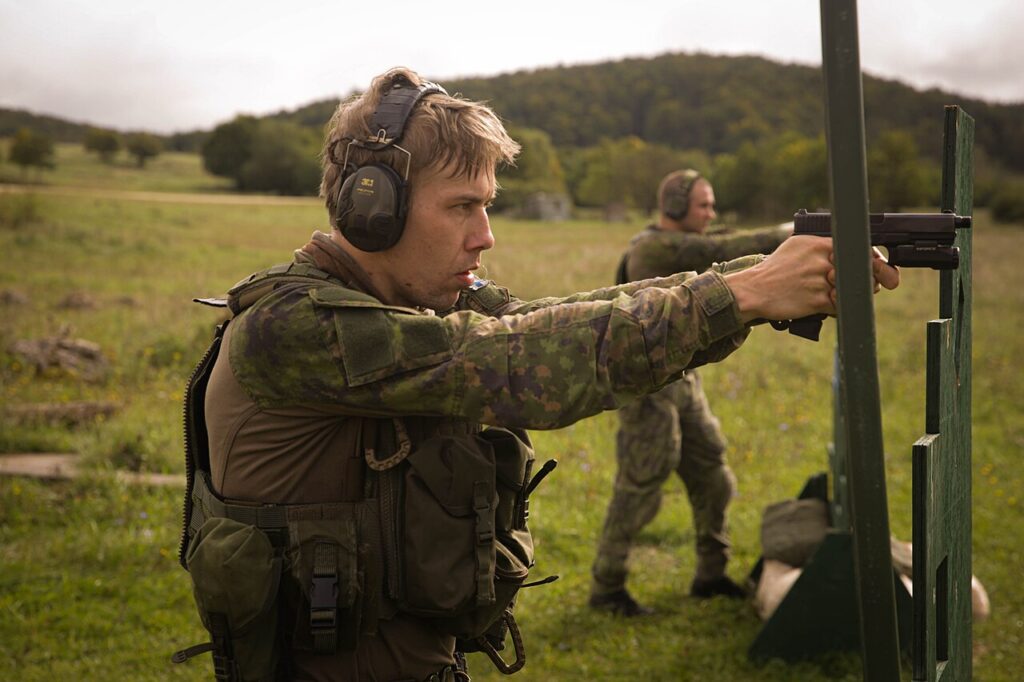 A soldier wearing protective earmuffs while aiming a pistol at a firing range.