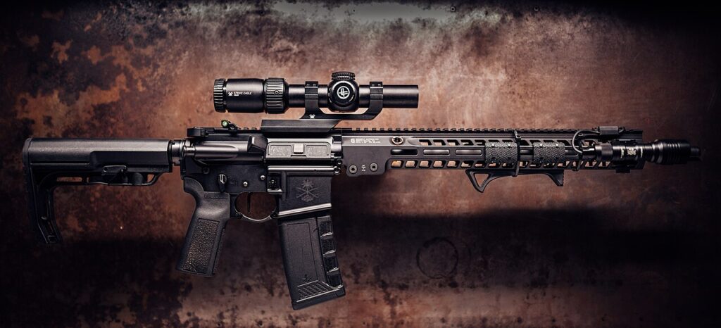 A modern black rifle equipped with a mounted variable power scope against a textured metal background.