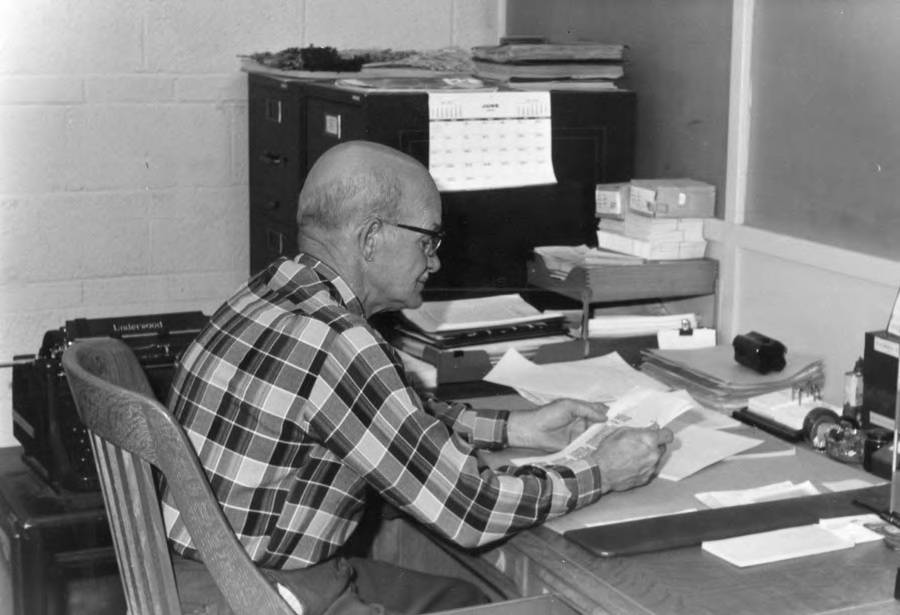 A person sitting at a desk reviewing paper documents and files, representing a manual, deliberate research process.