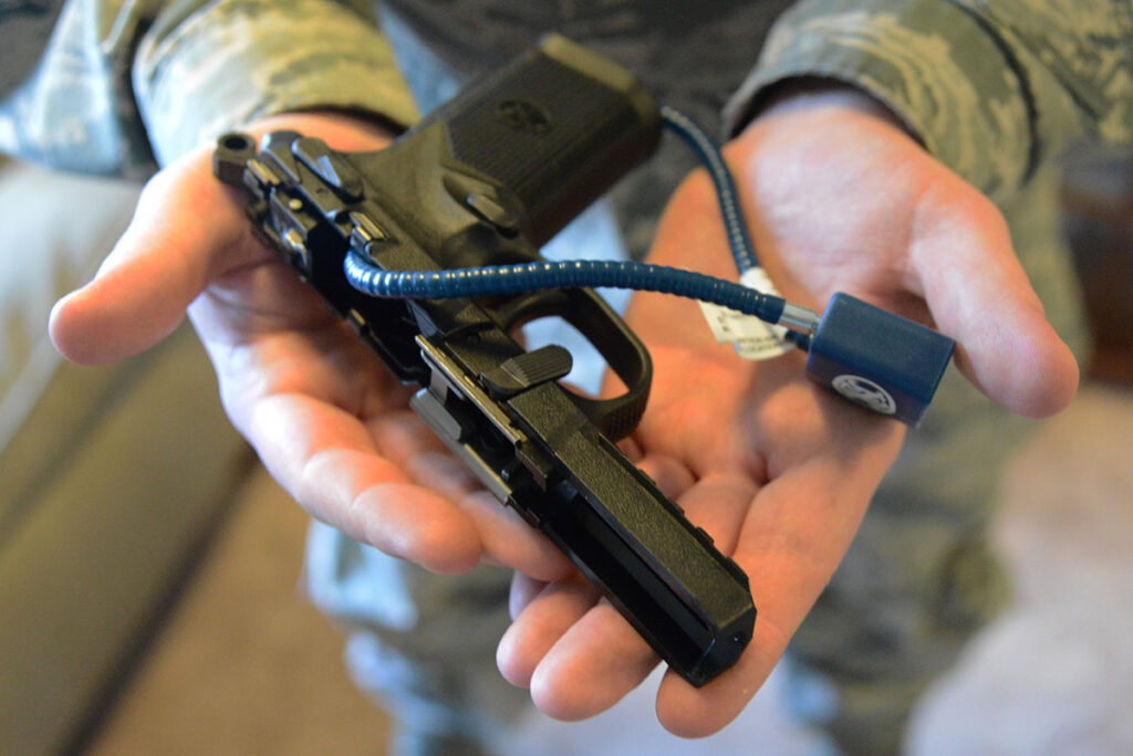 A person holding a modern handgun secured with a blue cable lock for safe storage and transport.